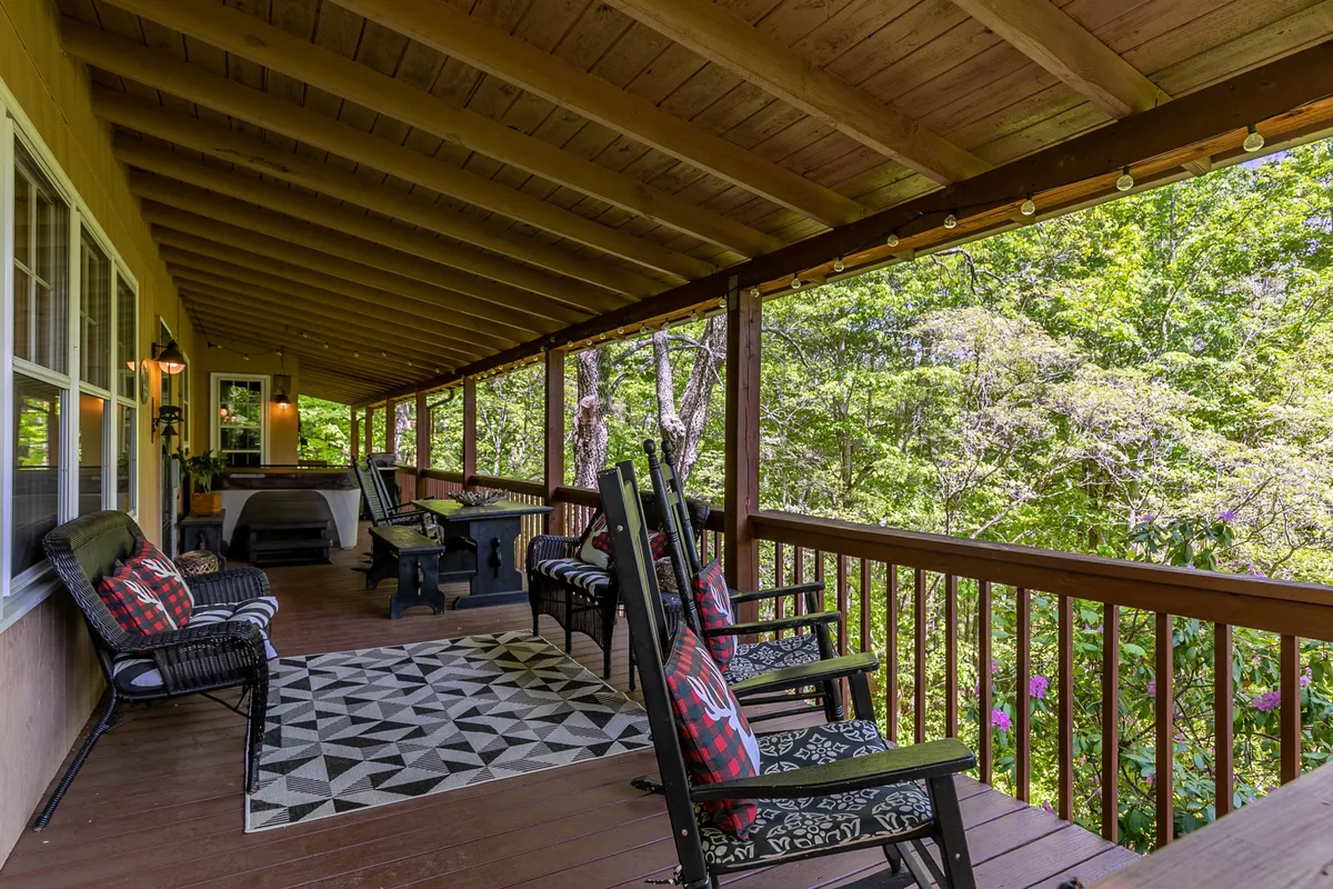 A cozy exterior porch scene with rocking chairs, a geometric patterned rug, wooden beams, lantern-style lighting, and lush greenery. The setup is perfect for morning coffee, reading, or stargazing, exuding tranquility and comfort.