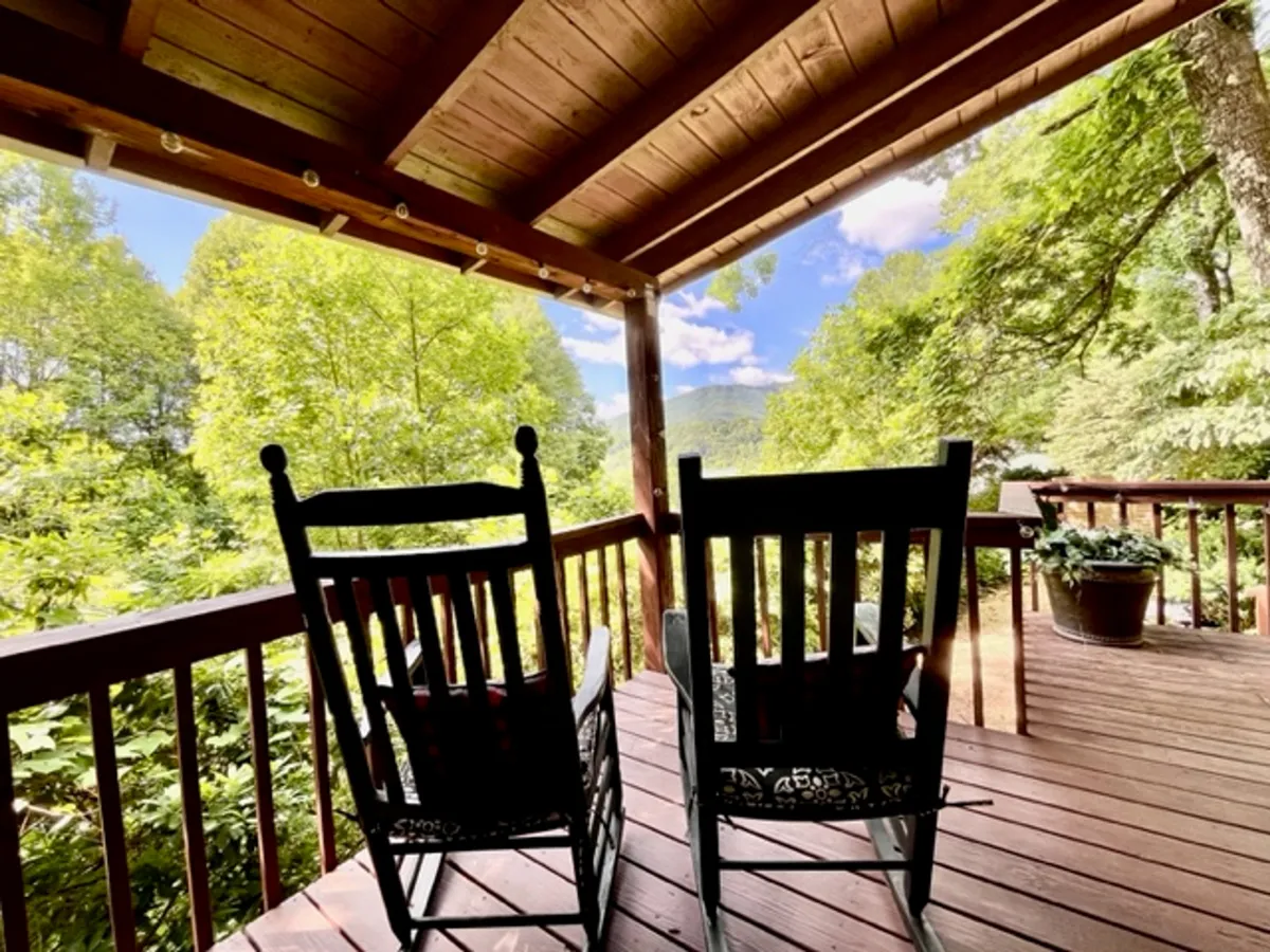 A peaceful exterior scene featuring rocking chairs set on a porch, surrounded by lush greenery and overlooking a distant mountain view. The chairs are positioned to take in the natural scenery, offering an inviting spot for relaxation, reading, or soaking up the views.
